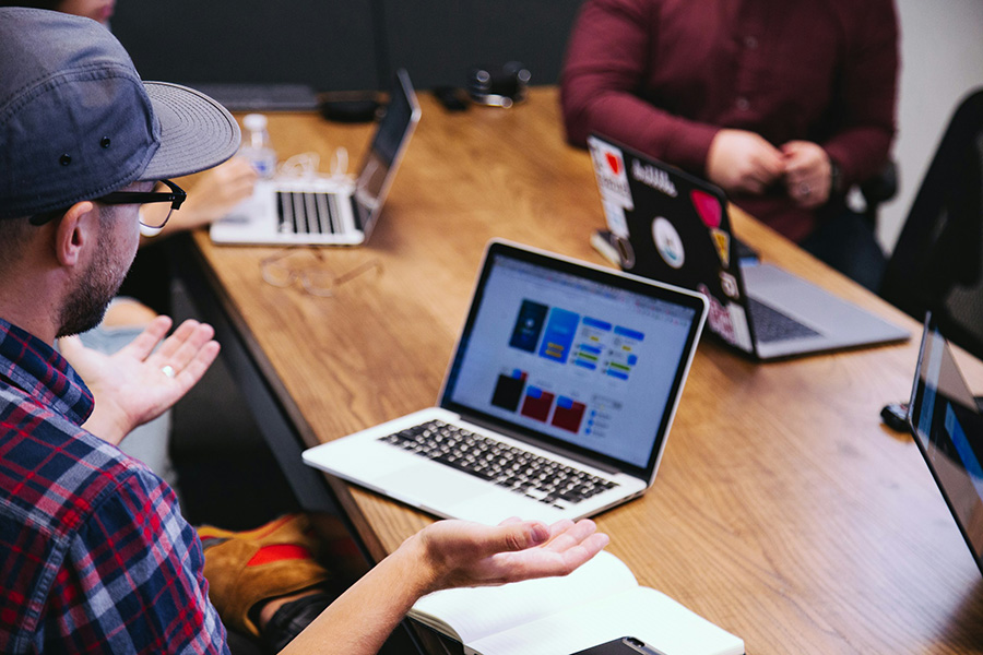 Das Foto zeigt eine Meetingsituation an einem Tisch, um den verschiedene Marketingexperten sitzen und sich zu einem Projekt austauschen. Auf dem Tisch stehen Laptops.